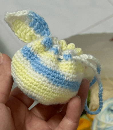 Pastel crochet drawstring pouch in Orange Bag style held outdoors — beginner project on crochet